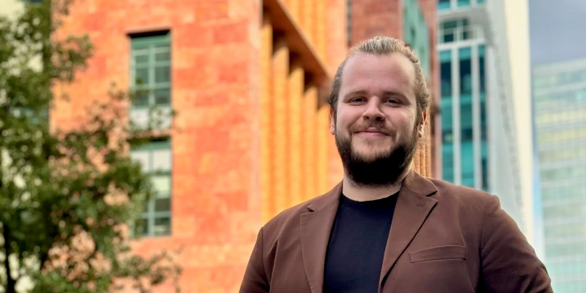 Mike Brachten in een bruin colbert voor een gebouw
